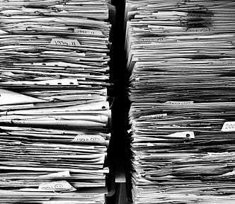 IMAGE: Two big stacks of paper files with a few labels, in black and white