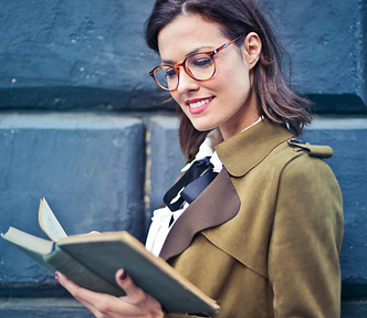 Woman in brown suede peacoat and glasses reading a book