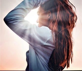 side view of girl with long red hair wearing long-sleeve top looking into sunny sky