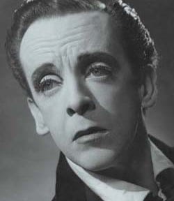 A black-and-white photograph of Robert Helpmann when he was younger. His face his pale, and his eyes are prominent. His expression is moody and haunting. He has short dark hair.