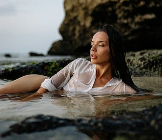 Sensual woman lying on sand in sea water.