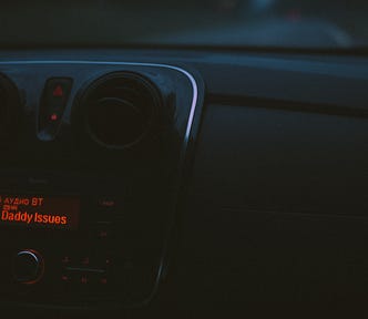 A car radio has the song title “Daddy Issues” on the screen in red.