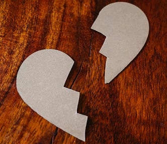 A cardboard cutout of a paper heart, ripped in two, sits on a wooden tabletop.