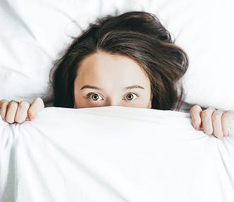 A woman lying on a bad with a scary eyes and blanket over half of her face