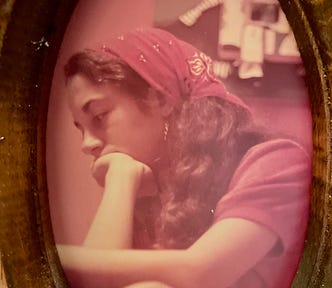 Framed faded photo of a young woman with long dark hair in a red kerchief with her chin in her hand.