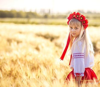 A girl in traditional Ukrainian attire stands in a wheat field. The poem featured in this article focuses heavily on the landscapes of Ukraine, particularly fields. The poem also focuses on a young girl with red ribbons in her hair and her journey to protect herself from outside forces. | Photo courtesy: Fokus_nik, Goodfon.