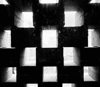 Concrete wall with a grid of square openings casting geometric shadows and light patterns from outside.