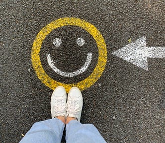 Person standing on a street with an arrow pointed to a painted yellow and white smiley face.