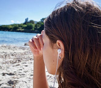 A young woman meditating on the beach with earphones listening to music