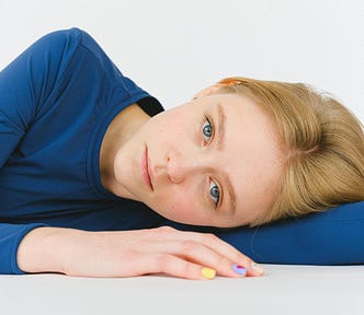 A woman with a somber expression, lying on her side on a white surface