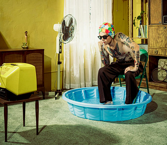 A man finds relief from the heat of summer with a swim cap and a kiddie pool in his living room