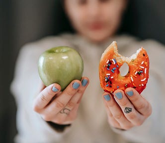 Woman showing apple and bitten doughnut