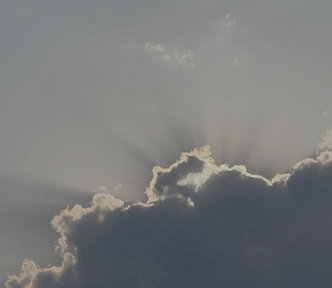 Sun’s rays peeking from behind fluffy clouds in late afternoon
