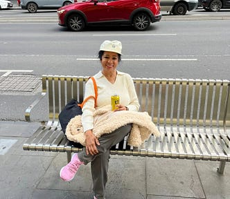 Woman sitting on a bench on the sidewalk with cars on a road on the background