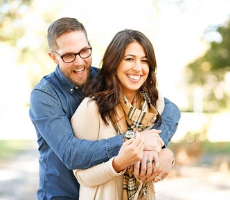 A picture of man who is hugging his wife, and they are both smiling.