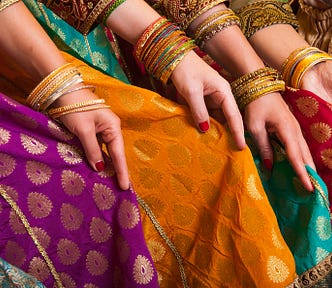 several women sitting in beautiful clothes from India, wearing gold bracelets