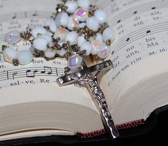 Color photo of a rosary and cross laying inside a hymnal.