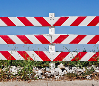 Photo of a red and white striped traffic barrier with blue sky in the background.