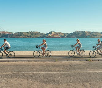 Four people riding a bike along the Tagus river.