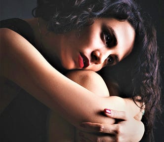 pensive woman with dark curly hair and red lipstick with head on knee and arms around legs