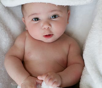 A cute baby wrapped in a white blanket, smiling up at the camera