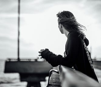 black and white photo of the author standing on a pier, looking out over the ocean