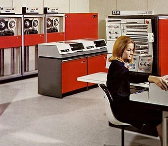 IBM System/360 promotional photo, ca. 1965. A woman sits at a terminal, surrounded by a System/360 with red panels.