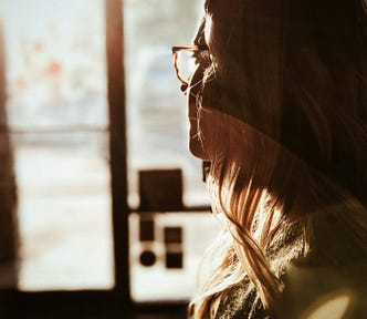 profile of a woman with long hair and glasses looking thoughtfully out of a window