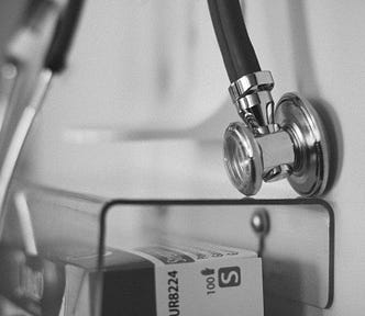 A black and white photo of a stethoscope hanging on a wall in a nondescript healthcare setting.