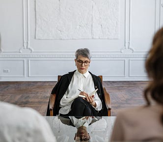 An elegant, professional, mature woman makes notes, while sitting across from a slightly younger man and woman who have some distance between them.
