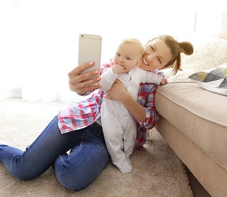 Mother holding a baby and taking a photo of them both.