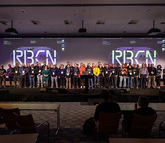 The speakers, workshop organizers and organizing team of the RoboCon 2024 on stage. Behind of this growd of roughly 40 people, there is the screen with RBCN logo.