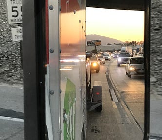 Side of U-Haul truck, traffic, side mirror, sunset. How Driving Cross Country in a Pandemic Made Our Marriage Stronger by Nancy Blackman. travel, cross country travel, driving cross country, pandemic