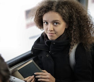 A young woman sitting on a bus, holding a book.