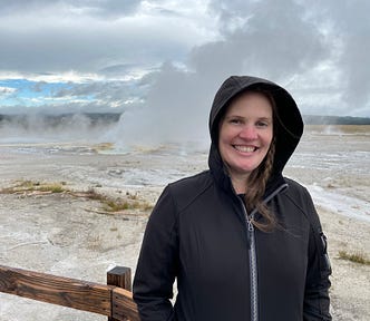 Jackie standing in black zipped hoodie in front of geyser.