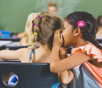 Schoolgirl whispering into her friend s ear in classroom at school