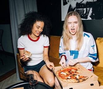 Two women eating pizza. They look like they’re having fun together. The image represents the idea that we give data away in everyday life without thinking. Free pizza, with a side of cyber vulnerability.