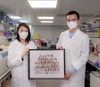 Dr Wong and Vincent stand in a laboratory holding a framed sketch of their colleagues