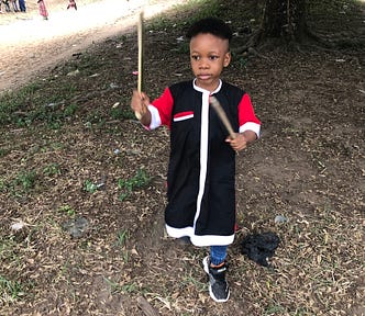 Little boy in red and black carrying two sticks.