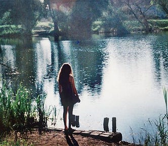 A photo of the back of a woman standing in front of a lake.