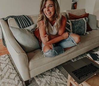 Girl on couch laughs with laptop and paper in front of her.