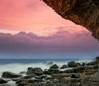 Edge of a sea cliff with rocks below, pink sky behind