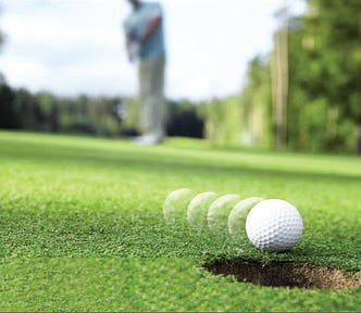 Golf ball rolling into the hole, out-of-focus golfer in the background