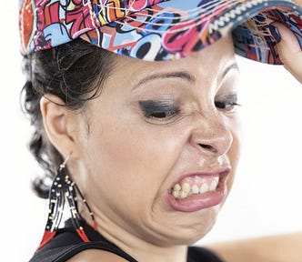 person in multi-colored baseball cap and eyeshadow makes a dramatic face of disgust