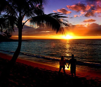 Beautiful brightly colored orange, yellow, purple, blue ocean beach sunset with black silhouettes of a palm tree and a couple (man & woman) holding hands in the suns reflection on the wet beach sand.