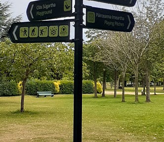 A pole with multiple signs in a park in English and Irish