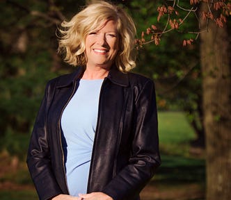 A picture of the author in a blue dress and black leather jacket. She is smiling.