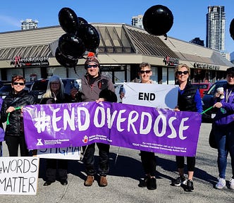 Members of the Tri-Cities Community Action Team are holding black balloons and a big purple sign with the words #End Overdose.