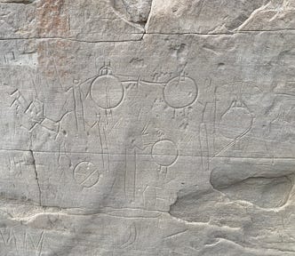 Multiple carvings of round objects with stick men standing behind them.