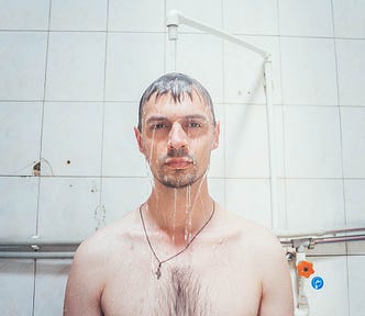A man stands under a shower head and looks at the camera